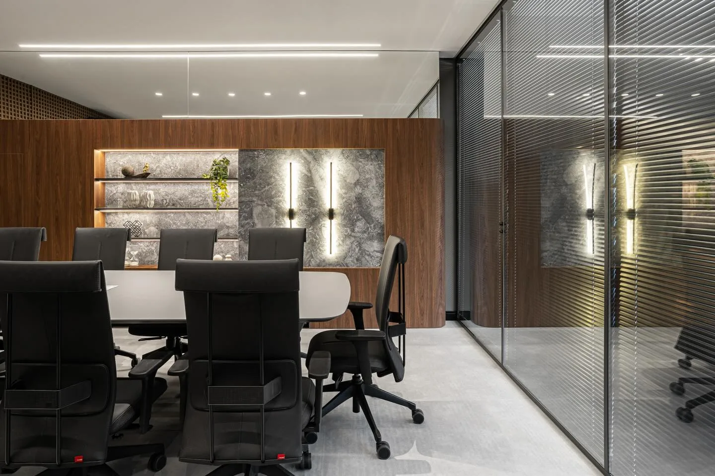 Sala de reunião corporativa com divisórias de vidro com persianas integradas, marcenaria em madeira e iluminação linear embutida